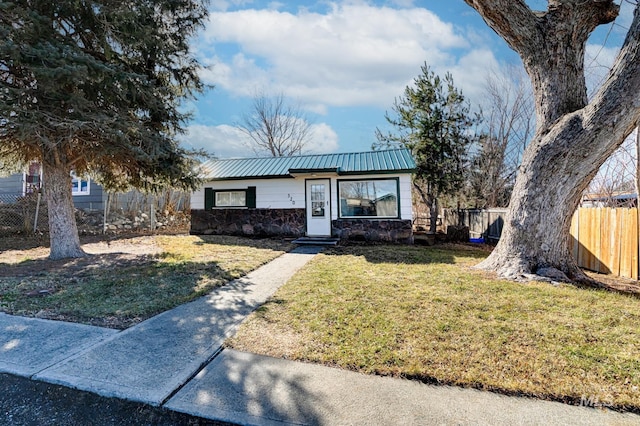 view of front of home with a front lawn, fence, stone siding, and metal roof