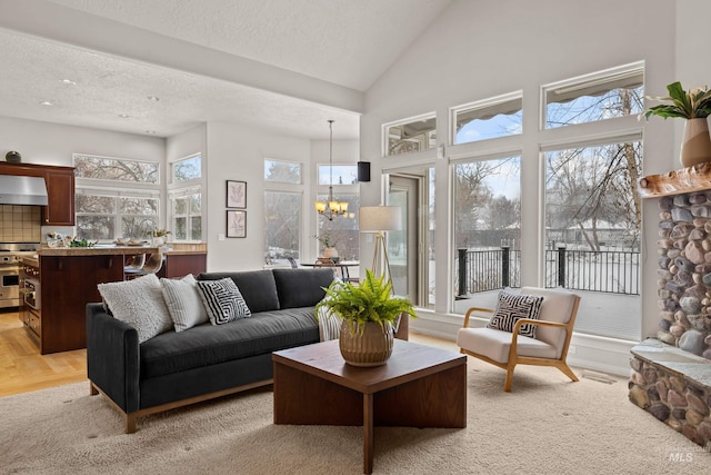 living room featuring an inviting chandelier, high vaulted ceiling, a textured ceiling, and light hardwood / wood-style flooring