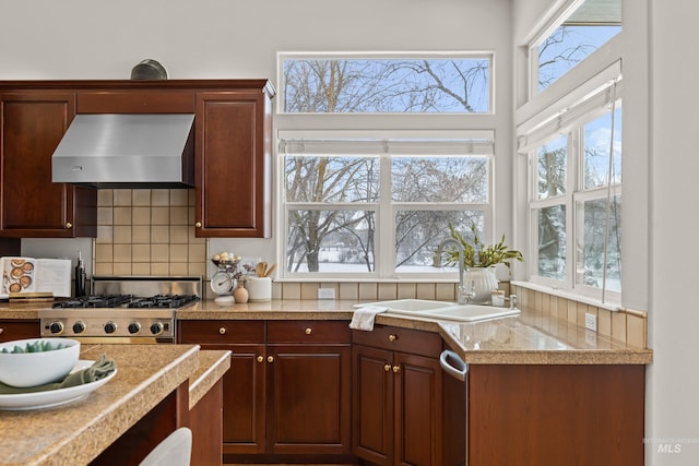 kitchen featuring wall chimney exhaust hood, sink, stainless steel stove, a wealth of natural light, and backsplash