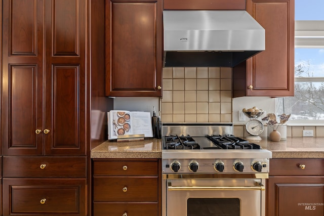 kitchen with high end stainless steel range oven, exhaust hood, light stone counters, and decorative backsplash