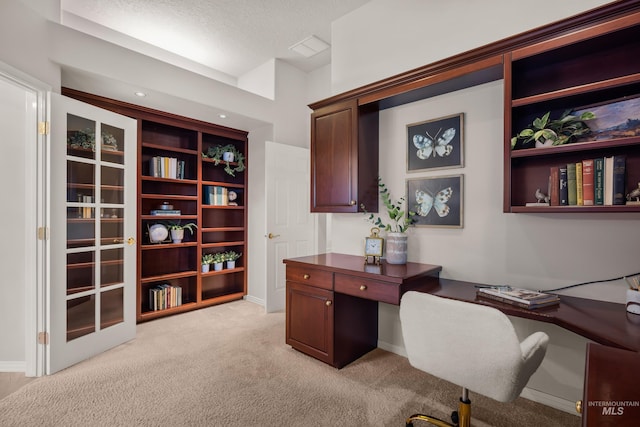 office space featuring light colored carpet, built in desk, and a textured ceiling