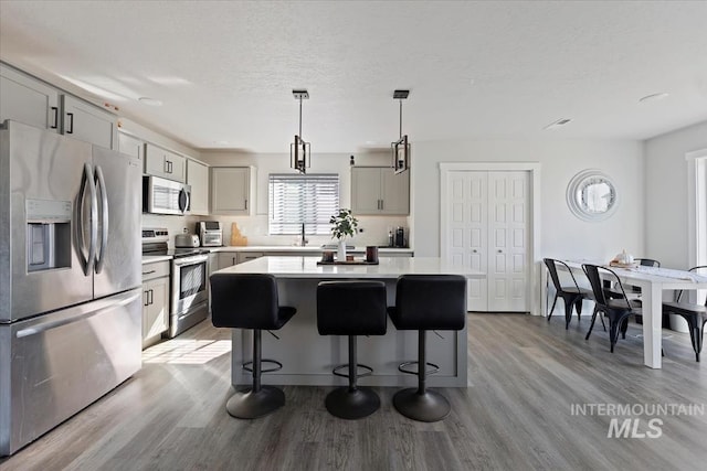 kitchen featuring a kitchen bar, a kitchen island, stainless steel appliances, light wood-style floors, and light countertops