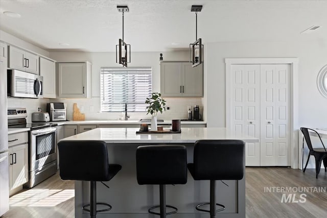 kitchen with light wood finished floors, appliances with stainless steel finishes, a breakfast bar, and light countertops