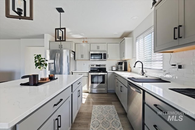 kitchen featuring gray cabinets, a sink, dark wood finished floors, a center island, and appliances with stainless steel finishes