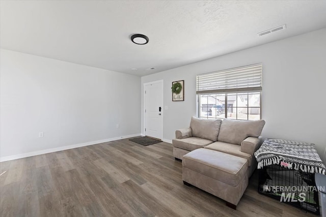 living area featuring visible vents, a textured ceiling, baseboards, and wood finished floors