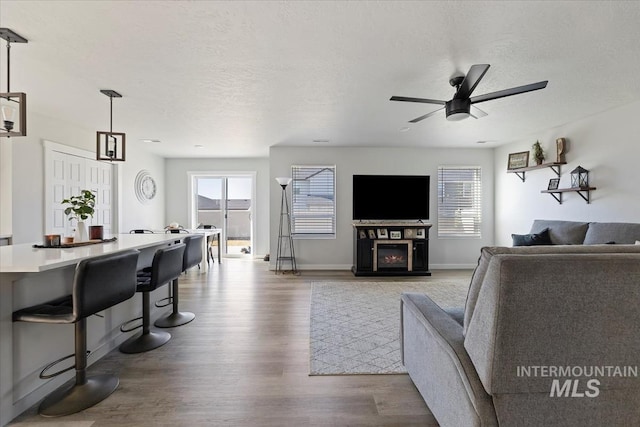 living room with wood finished floors, baseboards, ceiling fan, a textured ceiling, and a glass covered fireplace