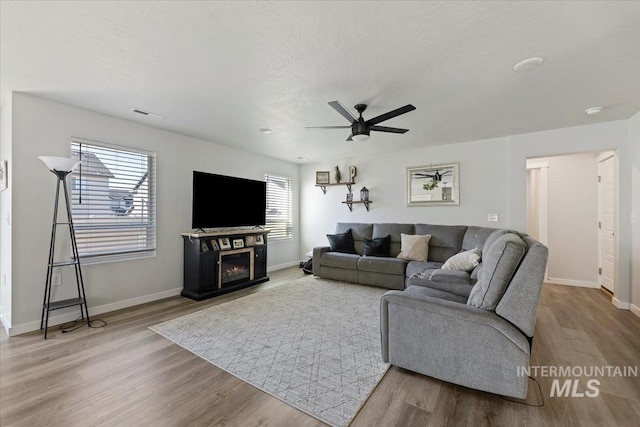 living area featuring wood finished floors, baseboards, a warm lit fireplace, and a textured ceiling