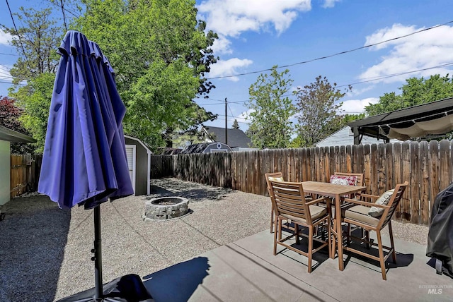 view of patio with an outdoor fire pit, a fenced backyard, outdoor dining area, and a storage unit