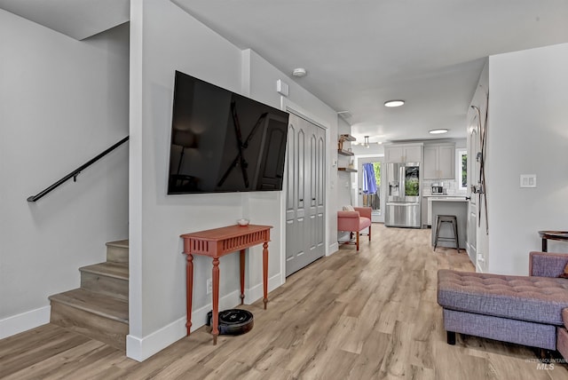 living area with light wood finished floors, stairway, and baseboards