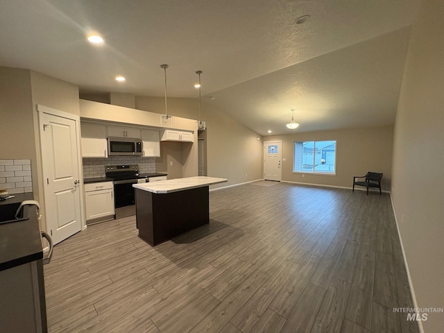 kitchen with vaulted ceiling, wood-type flooring, stainless steel appliances, a center island, and pendant lighting