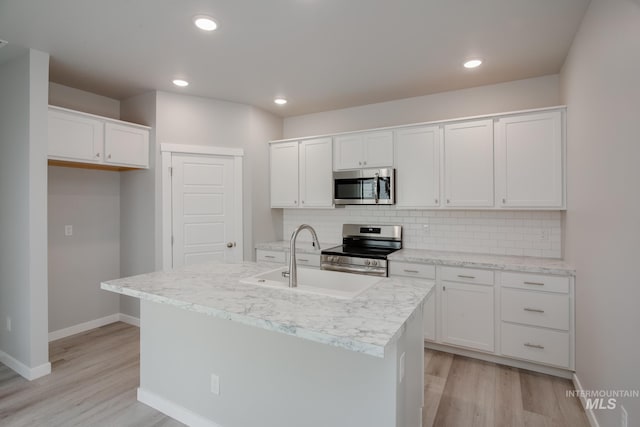 kitchen with a kitchen island with sink, stainless steel appliances, sink, light wood-type flooring, and white cabinets