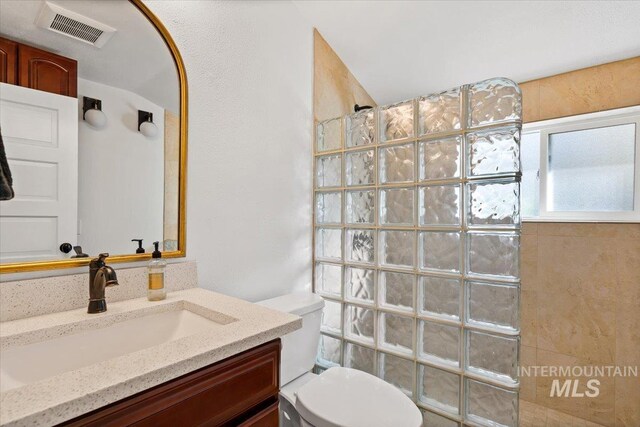 bathroom with toilet, a walk in shower, vanity, and visible vents