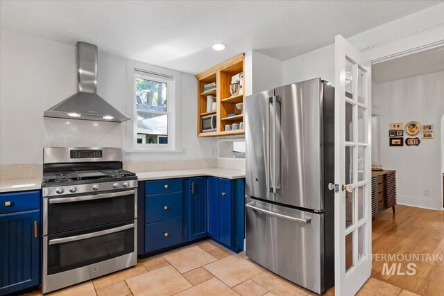 kitchen featuring blue cabinets, wall chimney range hood, light countertops, and appliances with stainless steel finishes