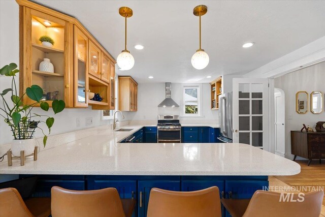 kitchen featuring open shelves, blue cabinets, a sink, appliances with stainless steel finishes, and wall chimney exhaust hood