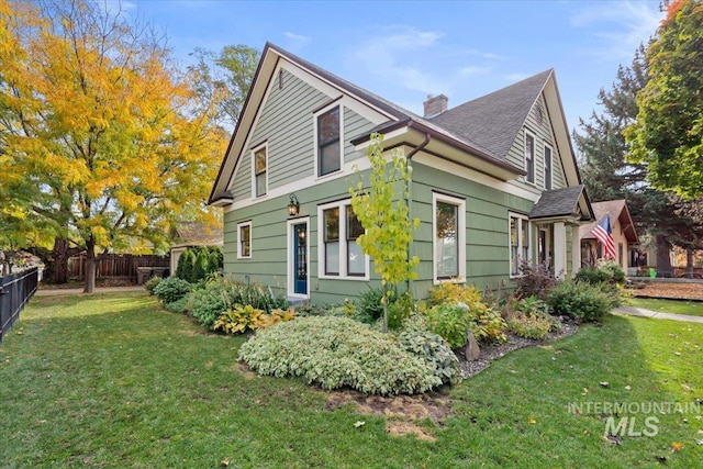 view of side of home featuring a yard, roof with shingles, fence, and a chimney