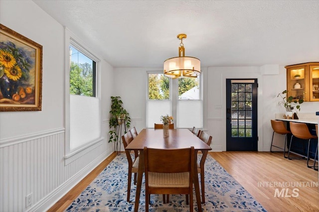 dining area featuring a textured ceiling, a notable chandelier, light wood-style floors, and wainscoting