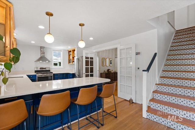 kitchen with light wood-type flooring, french doors, stainless steel appliances, blue cabinets, and wall chimney range hood