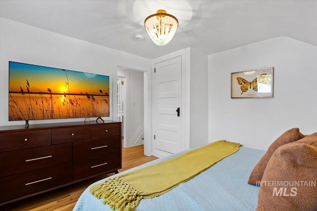 bedroom featuring a notable chandelier, lofted ceiling, and wood finished floors