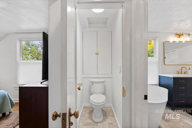 bathroom with a textured ceiling, a soaking tub, baseboards, toilet, and vanity