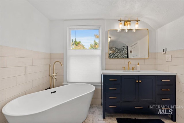 bathroom featuring a soaking tub, vanity, tile walls, and a textured ceiling