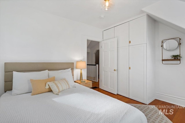 bedroom with baseboards, lofted ceiling, and wood finished floors