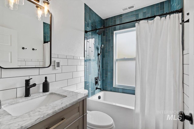 full bath featuring tile walls, visible vents, toilet, vanity, and shower / bath combo with shower curtain