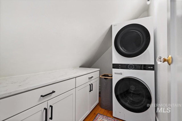 washroom with stacked washer and clothes dryer, cabinet space, and light wood-type flooring