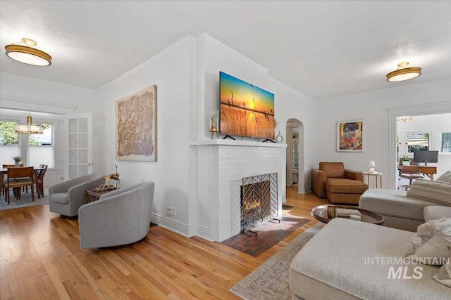 living area with baseboards, light wood-type flooring, arched walkways, and a fireplace