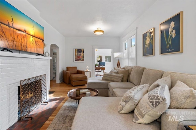 living room featuring arched walkways, a fireplace, and wood finished floors
