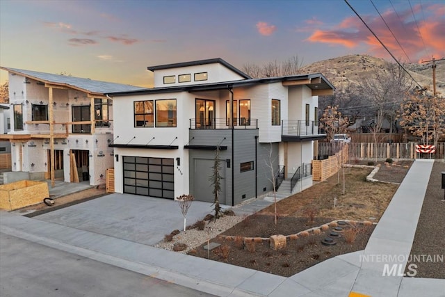 contemporary house with driveway, an attached garage, fence, and a balcony