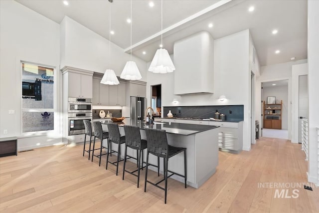 kitchen featuring gray cabinetry, stainless steel appliances, a sink, light wood-type flooring, and dark countertops