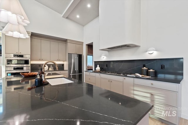 kitchen featuring stainless steel appliances, tasteful backsplash, custom range hood, a high ceiling, and a sink