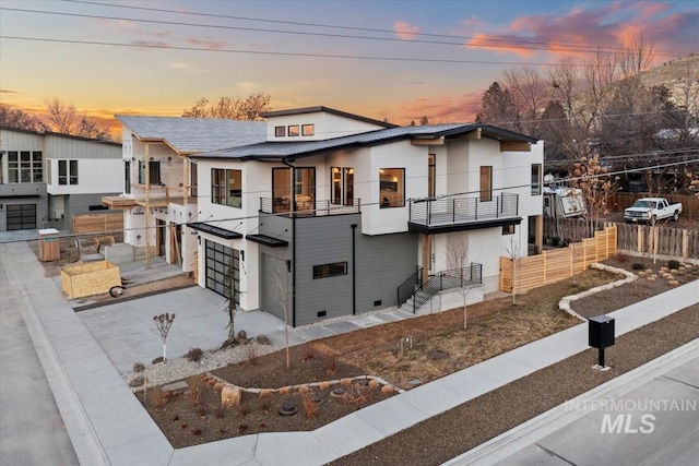 view of front of house with concrete driveway, fence, a balcony, and an attached garage