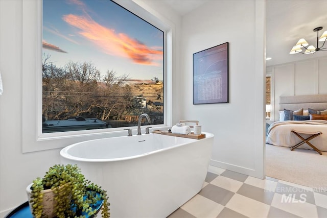 ensuite bathroom with a chandelier, ensuite bathroom, a freestanding tub, baseboards, and tile patterned floors