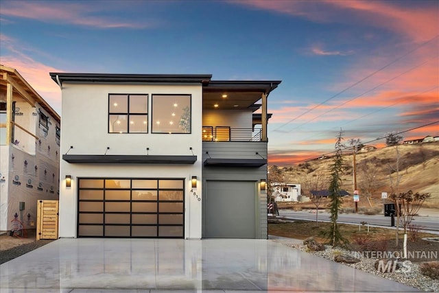 contemporary house with a garage, concrete driveway, a balcony, and stucco siding