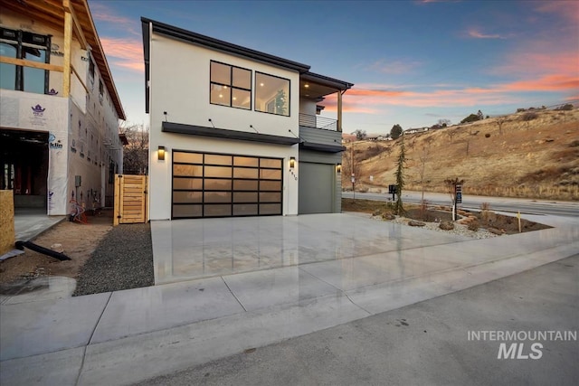 contemporary home with a garage, driveway, a balcony, and stucco siding