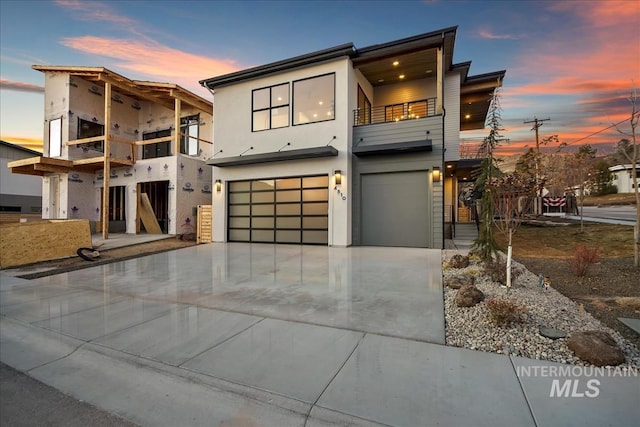 contemporary house with driveway, an attached garage, a balcony, and stucco siding