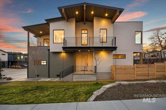 modern home featuring a front lawn, fence, and a balcony