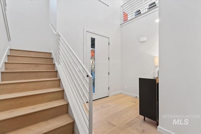 staircase featuring a high ceiling, baseboards, and wood finished floors