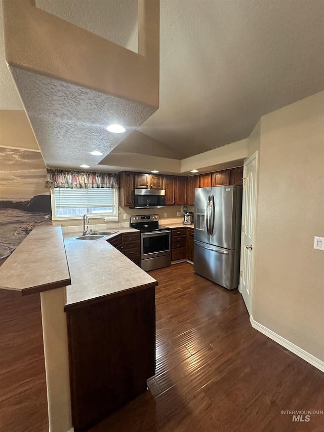 kitchen with a breakfast bar, sink, dark hardwood / wood-style flooring, kitchen peninsula, and stainless steel appliances