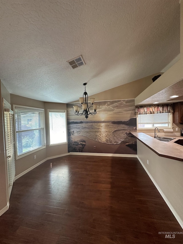 unfurnished dining area with an inviting chandelier, dark hardwood / wood-style flooring, sink, and a textured ceiling