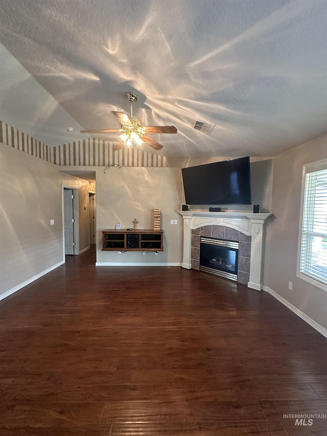 unfurnished living room with ceiling fan, dark hardwood / wood-style flooring, a tiled fireplace, and a textured ceiling