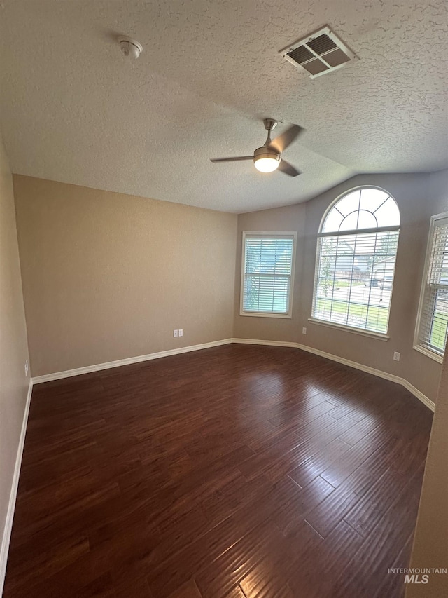 empty room with dark hardwood / wood-style flooring, ceiling fan, vaulted ceiling, and a textured ceiling