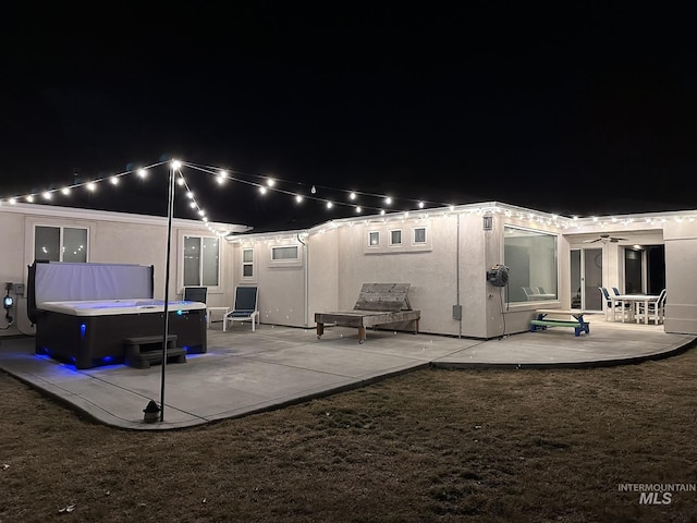 back of house at night with a yard, a patio, and stucco siding