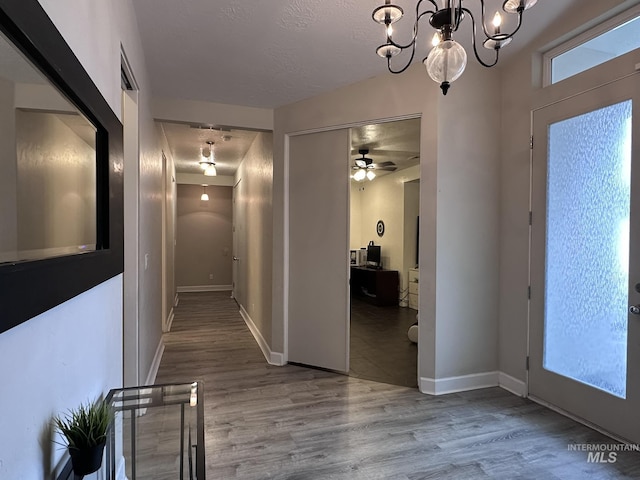 hall featuring baseboards, a textured ceiling, wood finished floors, and a notable chandelier