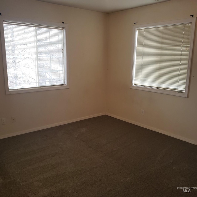 spare room featuring dark colored carpet and baseboards