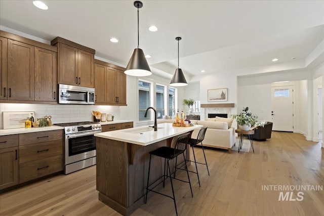 kitchen featuring a sink, light wood-style floors, light countertops, appliances with stainless steel finishes, and backsplash