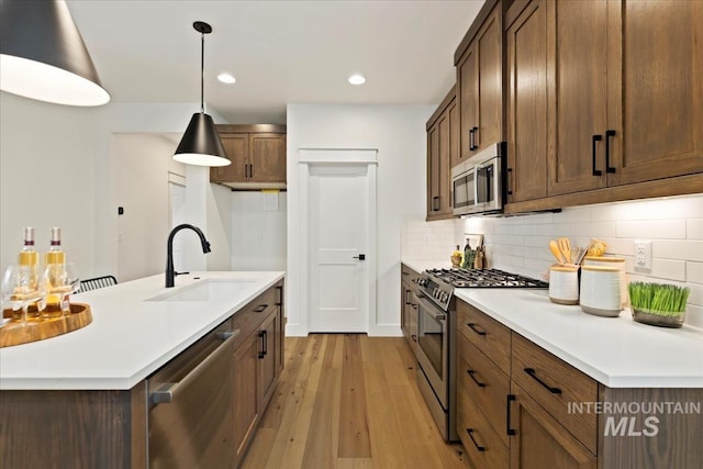 kitchen with a sink, light countertops, appliances with stainless steel finishes, decorative backsplash, and light wood finished floors