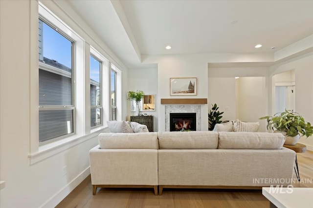 living area featuring recessed lighting, light wood-type flooring, a glass covered fireplace, and baseboards