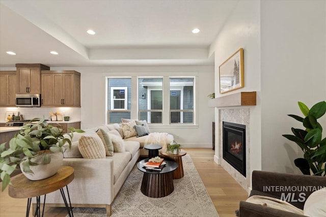 living room featuring baseboards, light wood finished floors, a high end fireplace, and recessed lighting